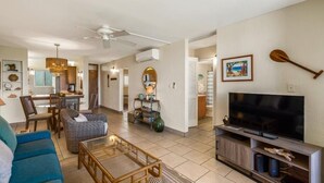 A living room with a television, seating, a dining area, and a kitchen in the background. - Menehune Shores #423 2 Bedroom Condo by RedAwning (Kihei)