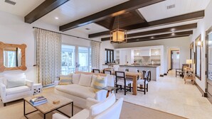 A spacious living area with a sofa, coffee table, and dining table. A kitchen is visible in the background.