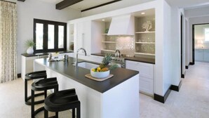 A modern kitchen with a central island, bar stools, and a decorative bowl of fruit.