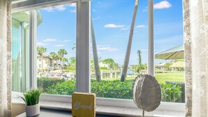 A window with a view of a resort area, a potted plant, a 'Blessed' sign, and a decorative object. - Waterfront 2 Bed in Popular Olde Marco I Close to Snook Inn (Marco Island)