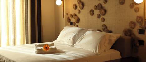 A neatly made bed with white linens and a towel with a flower, a wall with a textured pattern, and two wall-mounted lights.