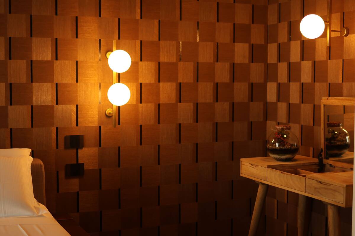 Une pièce avec un mur décoré de panneaux en bois, un lit, une petite table sur laquelle est posé un vase, et deux lampes fixées au mur.