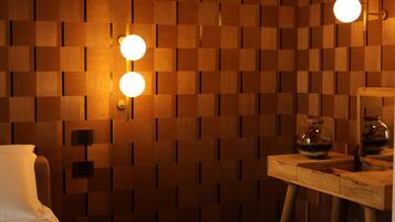 A room with a wooden wall panel design, a bed, a small table with a vase, and two wall-mounted lights.