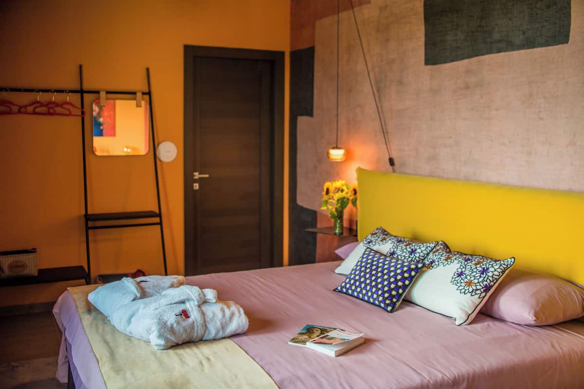 Un lit bien fait, avec des oreillers, une table de chevet sur laquelle repose un livre et un miroir fixé au mur.