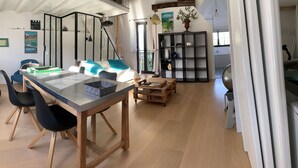 A modern living space with a dining area, a kitchen, and a staircase leading to a loft. - Loft Appart Proche Paris Chez Christine (Suresnes)