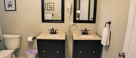 A bathroom with two sinks, a toilet, a trash bin, and a mirror.