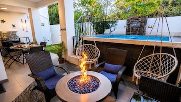 Un patio con un brasero, mobiliario de mimbre y una piscina.
