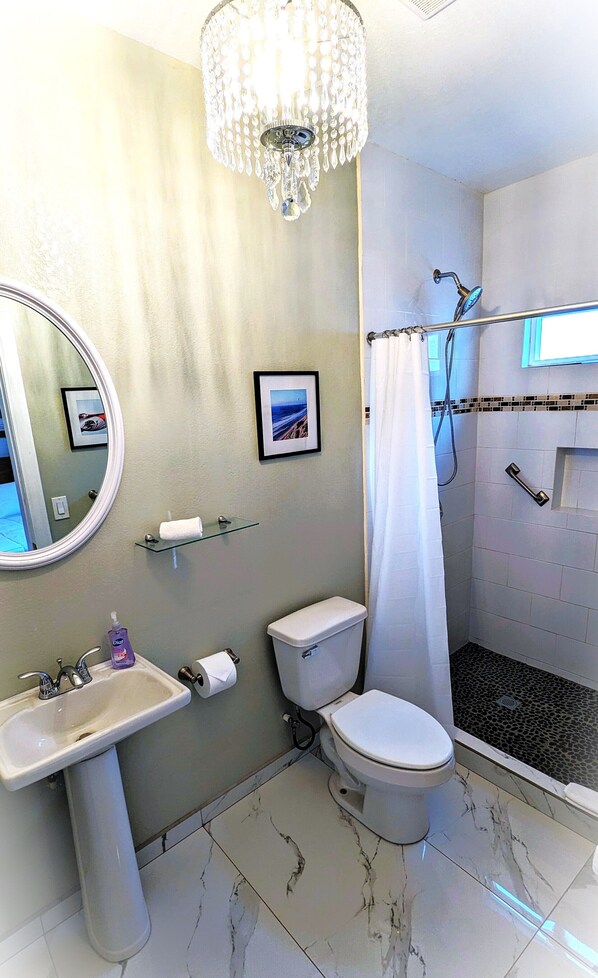 A bathroom with a sink, toilet, shower, and a chandelier.