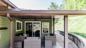 Un patio couvert, aménagé avec des meubles en osier, donnant sur le jardin arrière.