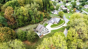 Vista aérea de um bairro residencial com uma casa, um amplo espaço para carros, um quintal cercado e um gramado bem cuidado.