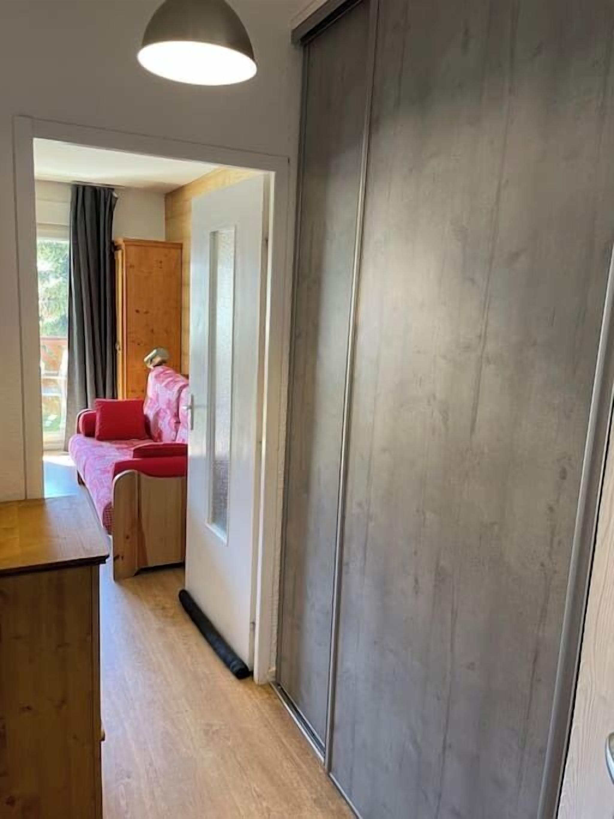 Un couloir avec un plancher en bois, une porte en métal et un canapé rouge à l’arrière-plan.