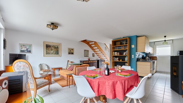 Ein geräumiger Wohnbereich mit Esstisch, Stühlen, einer Treppe und einer Küchenzeile.