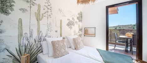 A bedroom with a large bed, a view of the outdoors through a sliding door, and a cactus-themed wall mural.