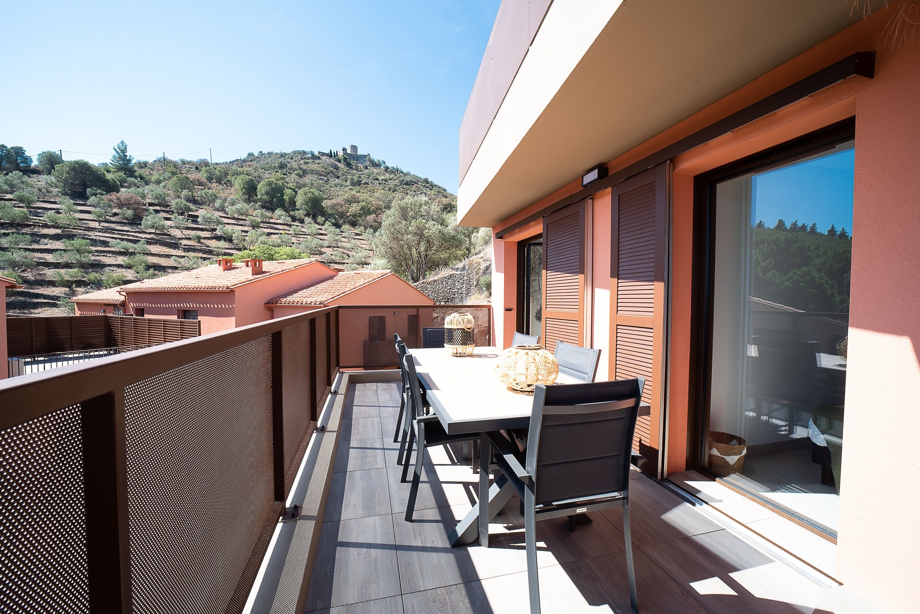 A balcony with a table and chairs, overlooking a hilly landscape.