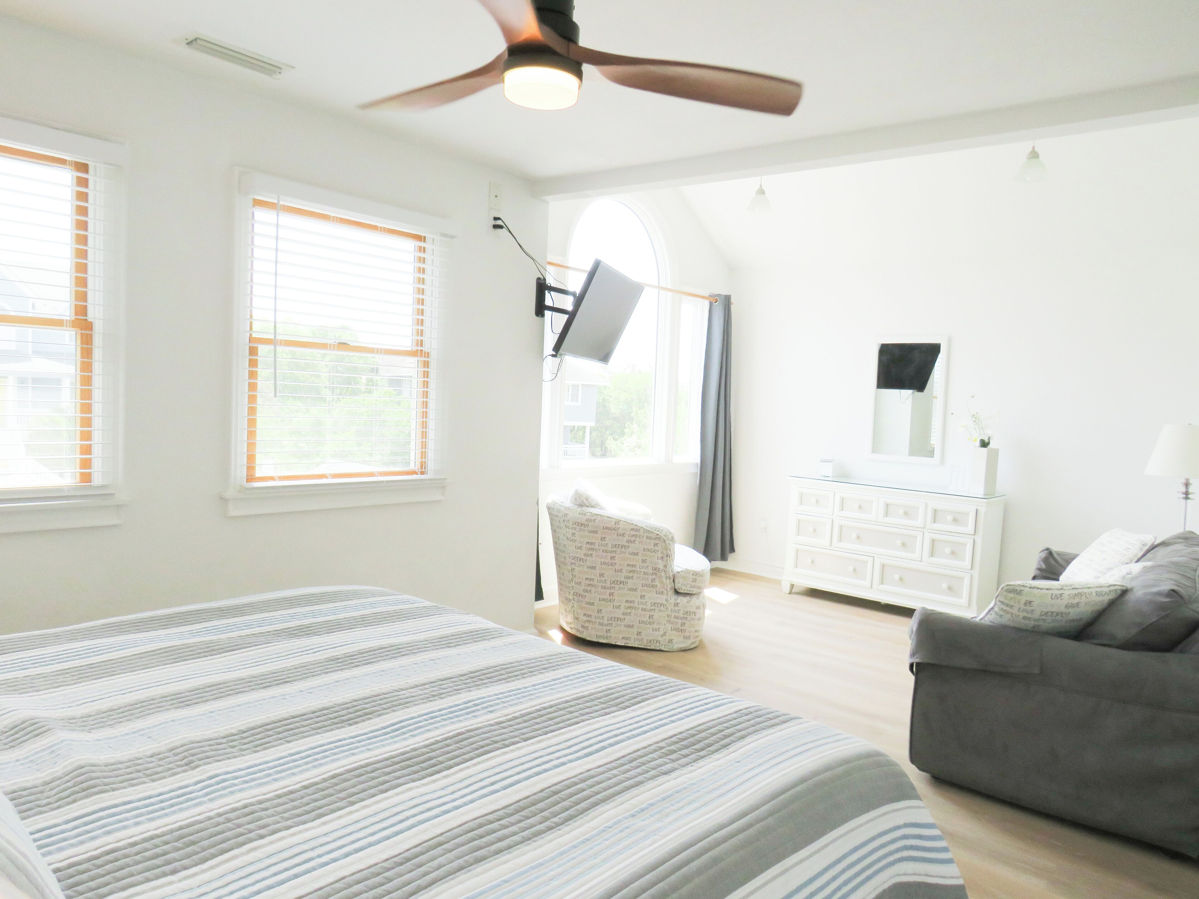 Ein Schlafzimmer mit einem Bett, einem grauen Sofa, einer weißen Kommode und einem Deckenventilator.