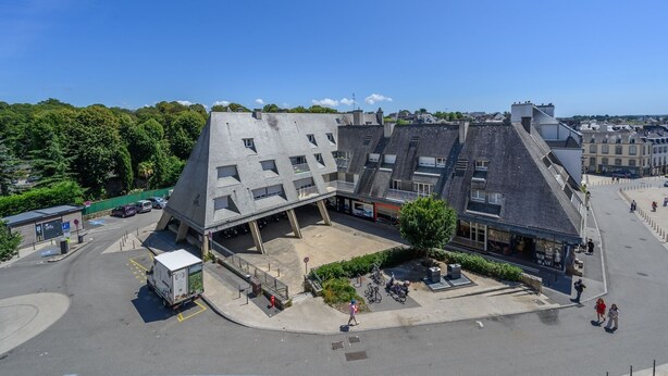 A multi-story building with a sloped roof, a central courtyard, and a parking area with a bus stop.