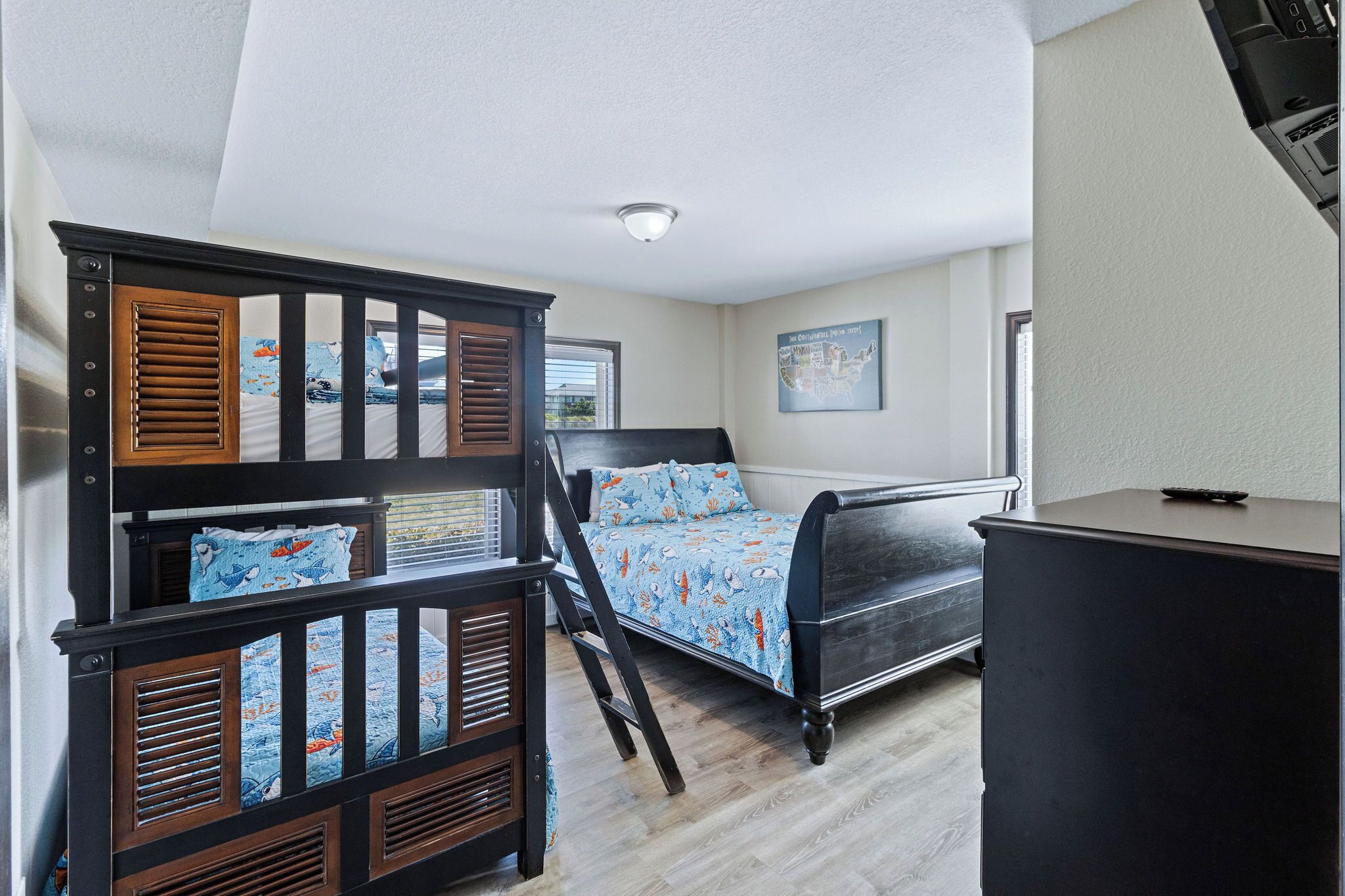 Une chambre avec un lit superposé, un bureau et un lit recouvert d’une couvre-lit à motifs.