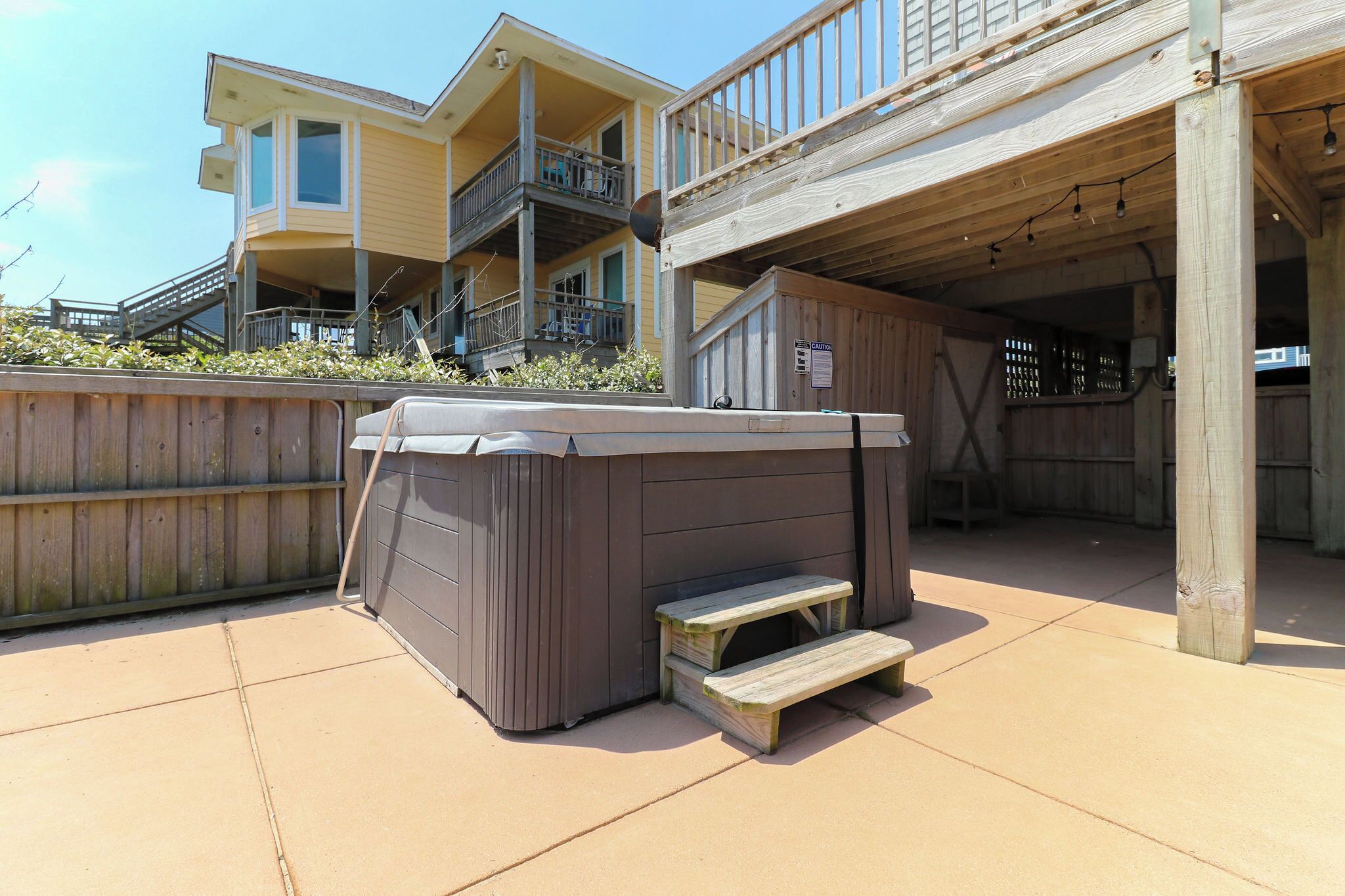A wooden deck with a hot tub and picnic table, overlooking a building with balconies.