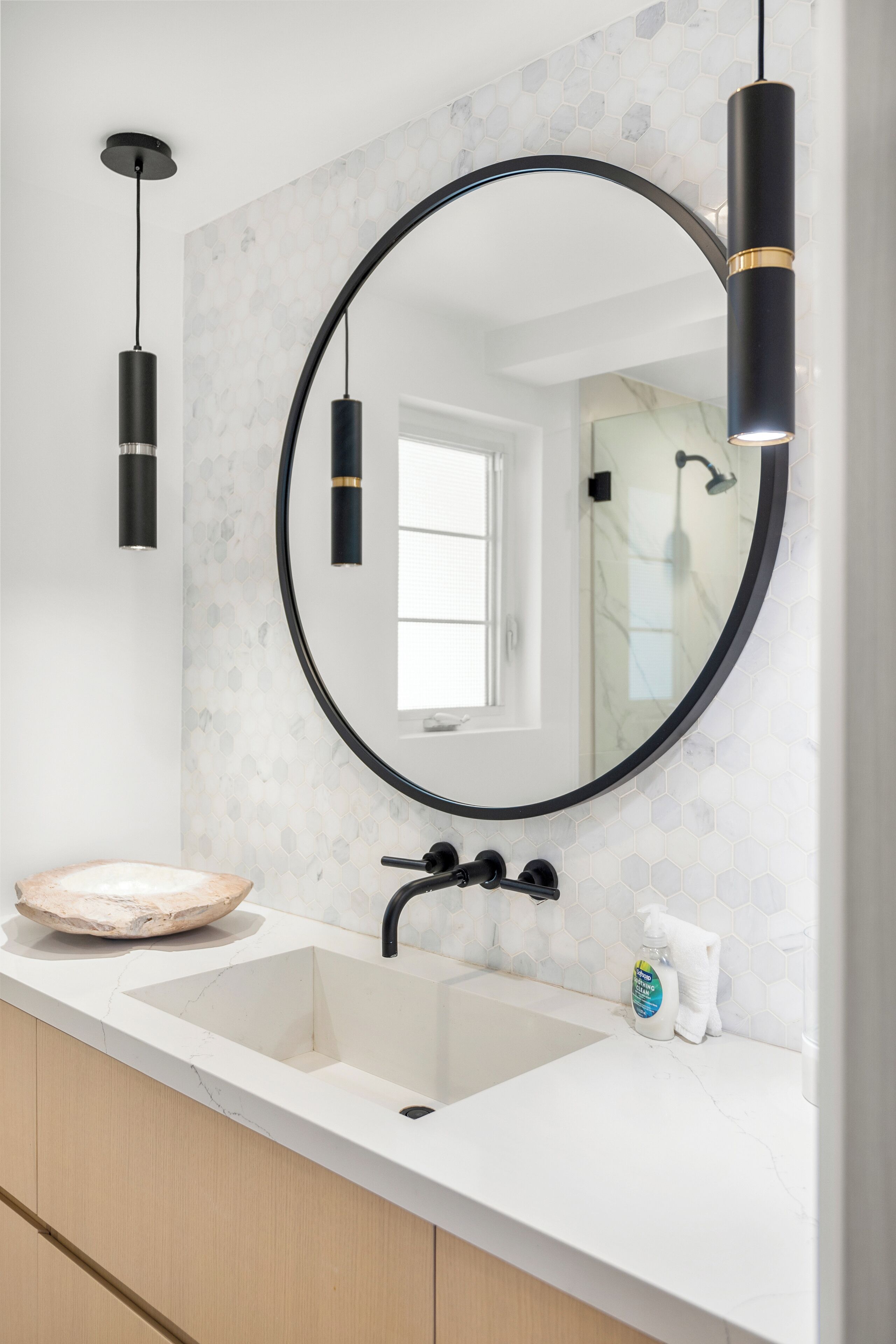 Un bagno con un lavandino bianco, uno specchio rotondo e una lampada a sospensione nera.