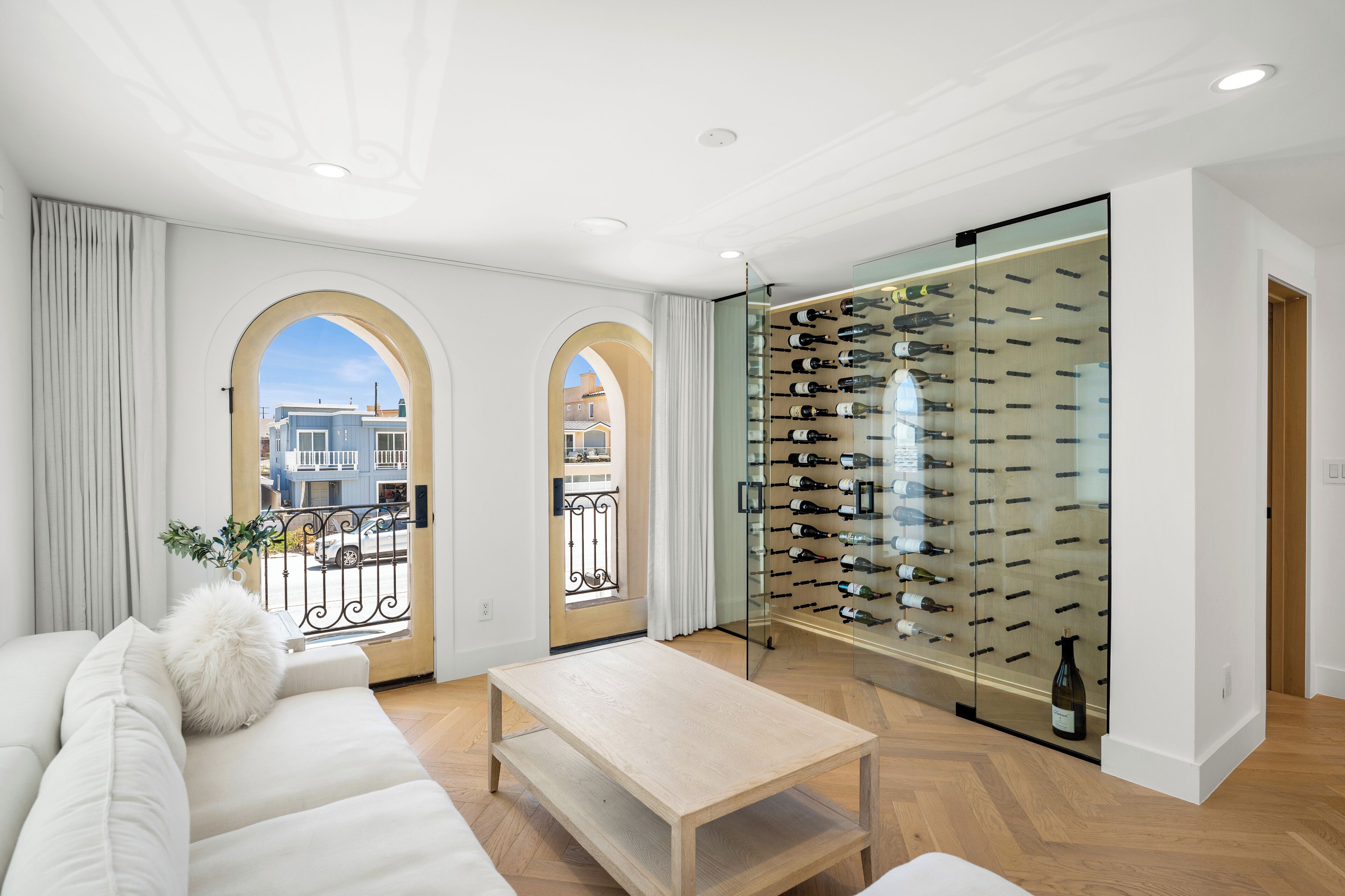 Una sala moderna con un sofá blanco, una mesa de centro de madera y una estantería para vinos con botellas.