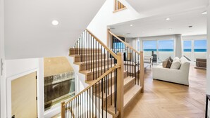 A spacious living area with a wooden staircase, a large window offering a view of the sea, and a modern interior design.