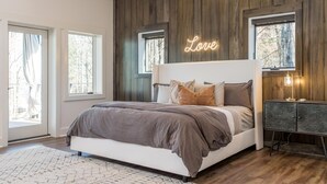 A modern bedroom with a large bed, wooden panel walls, and a neon 'Love' sign. - Long Range Mtn Views Next to Jump Off Rock! Ultra Modern, Very Unique Open Floor (Hendersonville)