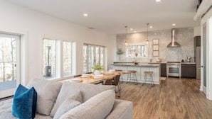 A modern kitchen with a central island, bar stools, and a dining area with a wooden table and chairs. - Long Range Mtn Views Next to Jump Off Rock! Ultra Modern, Very Unique Open Floor (Hendersonville)