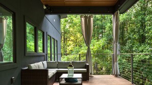 A balcony with a sofa, a table, and a lantern. - Long Range Mtn Views Next to Jump Off Rock! Ultra Modern, Very Unique Open Floor (Hendersonville)