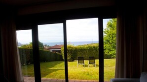Habitación con un amplio ventanal corredero que da a un jardín cuidado con una banca y vistas al mar.
