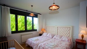 Un dormitorio con dos camas, ventanas amplias, una cuna y una mesita de noche con lámpara.