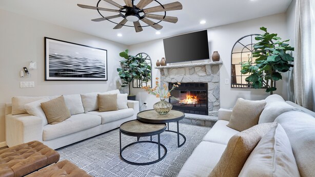 Un salon moderne avec un canapé blanc, deux tables rondes, une cheminée et un ventilateur de plafond.
