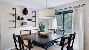 Un coin repas avec une table en bois foncé, six chaises, un saladier et un luminaire suspendu.