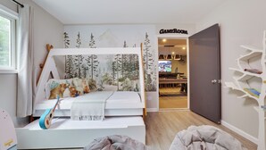 Une chambre avec un lit superposé, une guitare, une couverture et une fresque représentant des arbres et des montagnes.