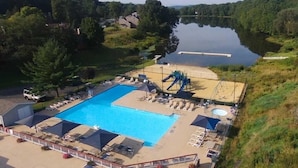Une piscine avec un toboggan et une plus petite piscine circulaire, entourée de chaises longues et de parasols.