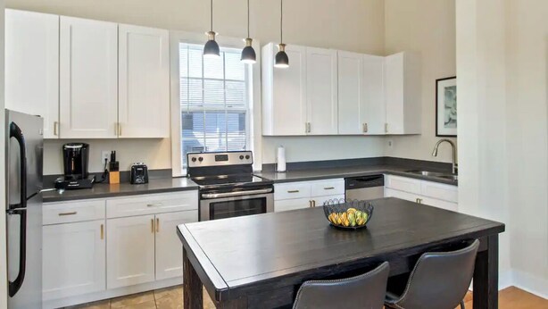 A modern kitchen with white cabinets, a black countertop, and a central island with chairs. - Cute 1bed walk to French Q & Bourbon St (New Orleans)