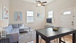 A living room with a grey sofa, a coffee table, a TV, and a dining table with a bowl. - Cute 1bed walk to French Q & Bourbon St (New Orleans)
