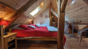 A cozy attic bedroom with a wooden ceiling, a bed with red bedding, a nightstand, and a window. - Duplex 6/8 Pers 90 m² Le Bez Serre Chevalier 1400 (La Salle-les-Alpes)