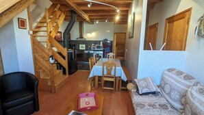 A cozy living room with a wooden staircase, a dining area, and a kitchen in the background. - Duplex 6/8 Pers 90 m² Le Bez Serre Chevalier 1400 (La Salle-les-Alpes)