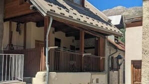 A two-story building with a wooden balcony, a stone wall, and a metal gate. - Duplex 6/8 Pers 90 m² Le Bez Serre Chevalier 1400 (La Salle-les-Alpes)