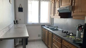 A kitchen with wooden cabinets, a stainless steel countertop, a built-in oven, and a window providing natural light. - Appartement : Le Petit Aubray (Châteauroux)