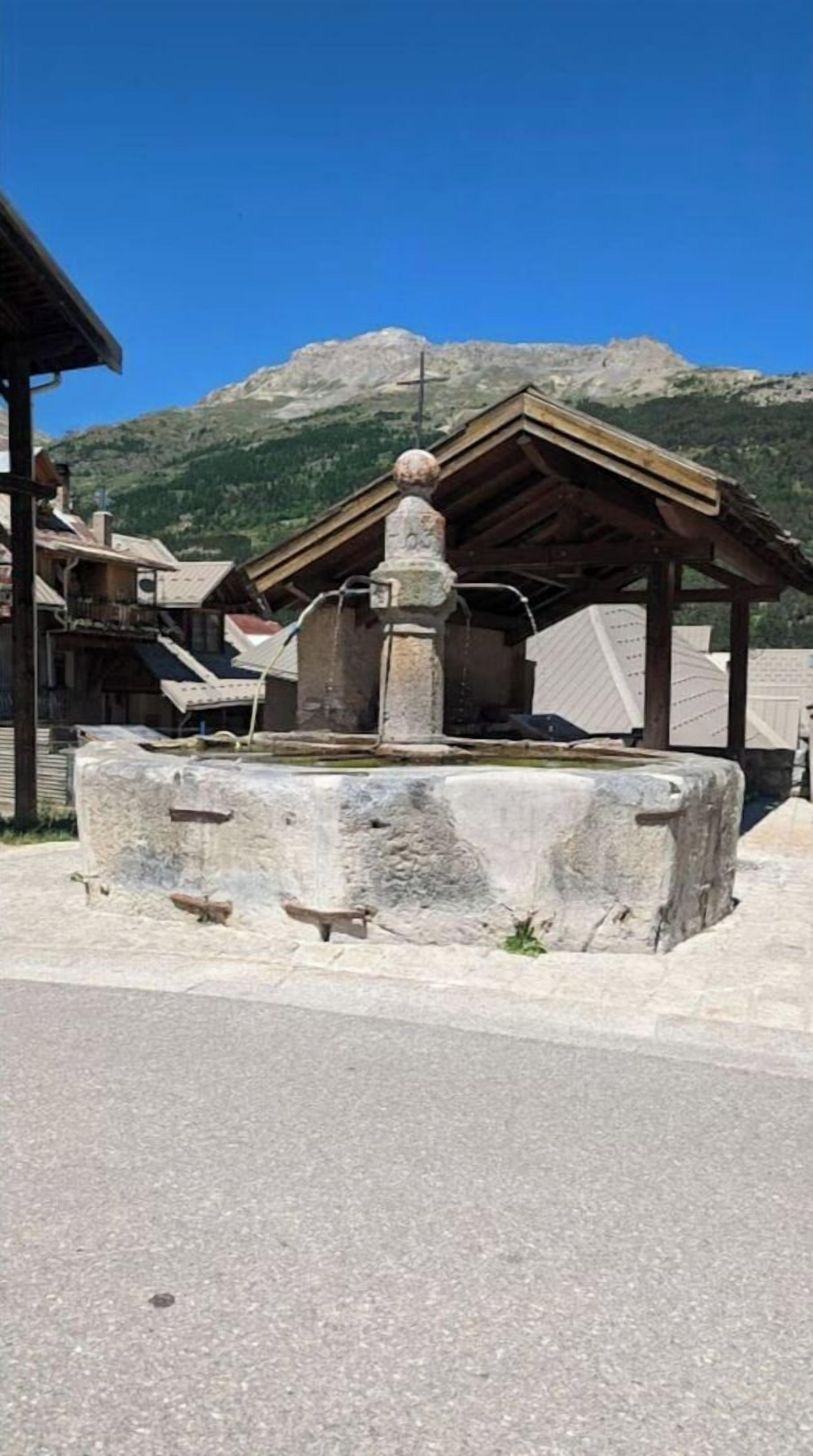 Una struttura in pietra con tetto di legno, forse un monumento storico o una piccola cappella, con montagne sullo sfondo.