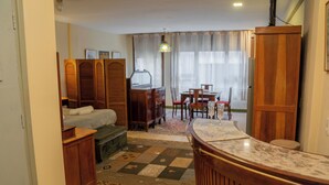 Een compacte hotelkamer met een bed, een klein bureau, een houten garderobe, een eettafel met stoelen en een kamerbreed tapijt met een patroon.