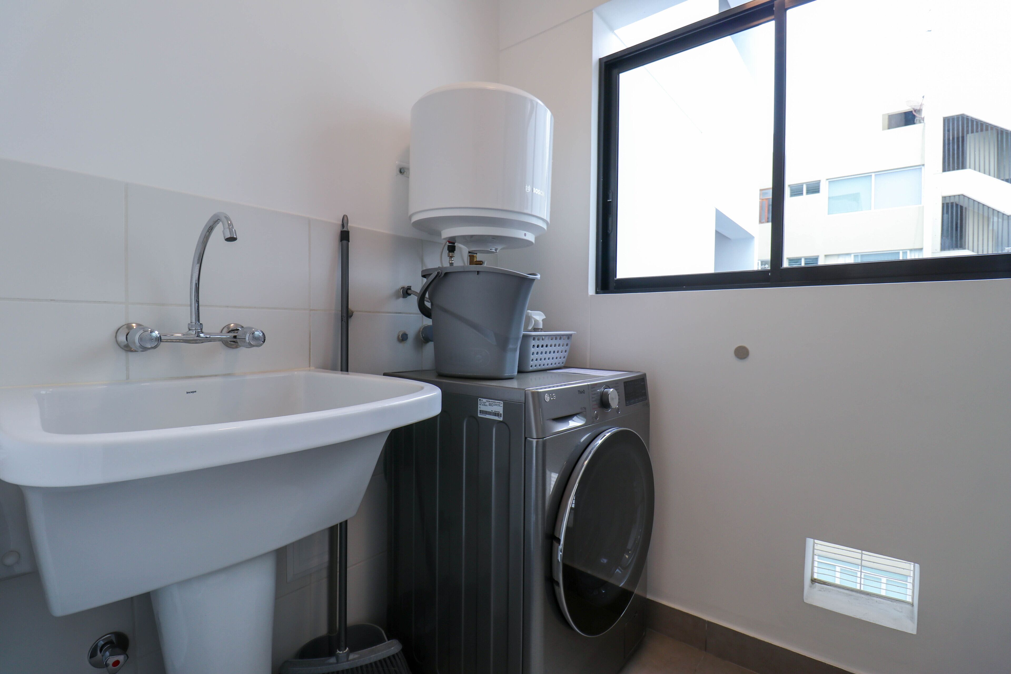 Une petite salle de bain équipée d’un lavabo, d’un lave-linge et d’une fenêtre qui laisse entrer la lumière naturelle.