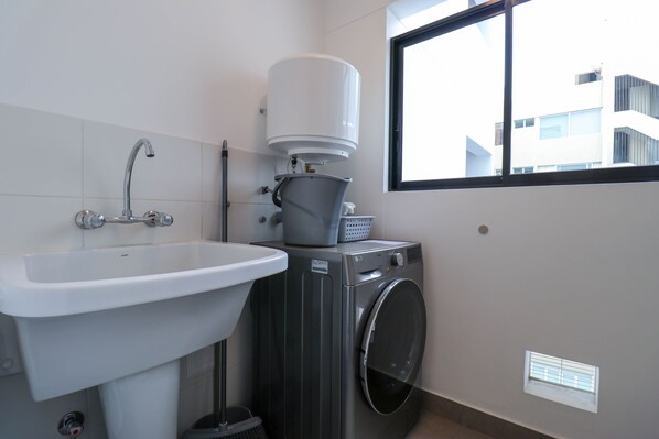 A compact bathroom with a sink, washing machine, and a window providing natural light.
