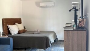 Ein Schlafzimmer mit einem Bett, einem blauen Sofa, einer Holzkommode und einer Klimaanlage.