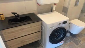 Ein kleines Badezimmer mit Waschmaschine, Waschbecken und Toilette.