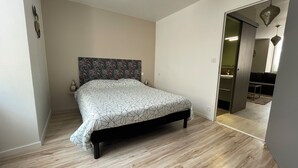 Ein Schlafzimmer mit einem Bett, Holzboden, einem gemusterten Kopfteil und einer Tür zu einem Badezimmer.