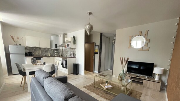 Ein modernes Wohnzimmer mit einem grauen Sofa, einem Glastisch und einem Fernseher.