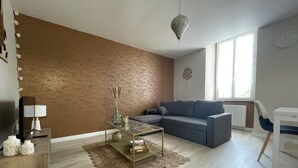 Ein modernes Wohnzimmer mit einem grauen Sofa, einem Glastisch und einer Wand mit brauner Struktur.