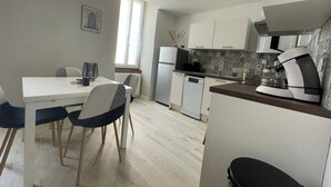 Eine kompakte Küche mit Essbereich, ausgestattet mit einem weißen Tisch, Stühlen, einem Kühlschrank, einem Geschirrspüler und einer Kaffeemaschine.